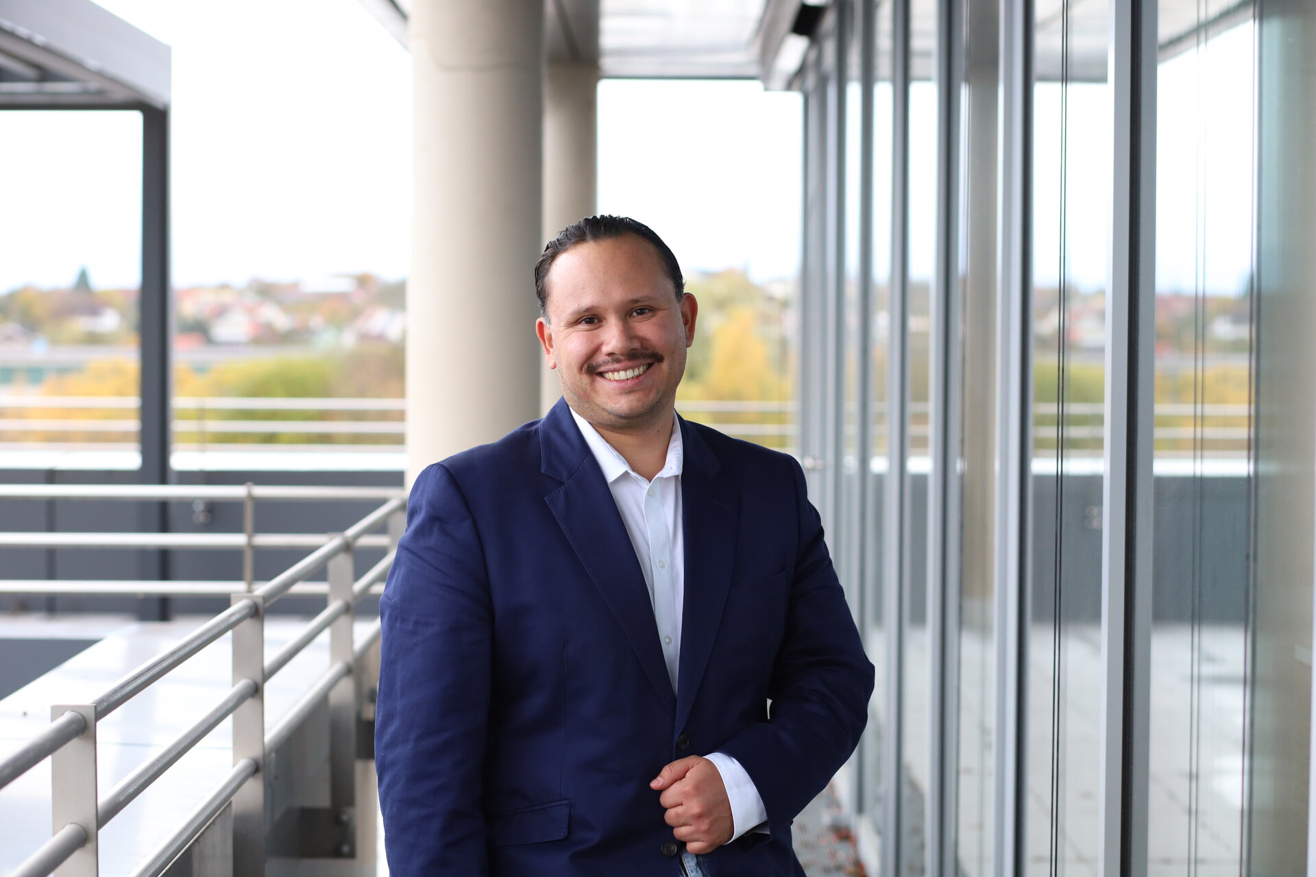 Ein Mann in einem blauen Anzug und weißem Hemd lächelt freundlich in die Kamera.